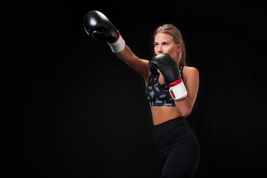Beautiful female athlete in boxing gloves, in the studio on a black background. The boxer fulfills the blow