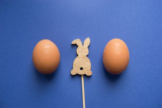 Easter background, eggs and a wooden hare on a blue background, flatlay, top view, empty space for text.
