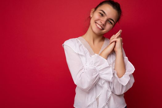 Young beautiful european stylish brunette woman wearing white blouse isolated over red background with positive sincere emotions. Simple and natural looking at the camera. Free space.