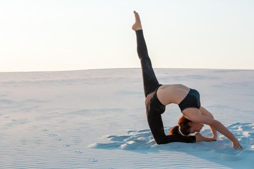 Fitness yoga woman stretching on sand. Fit female athlete doing yoga pose before running training outside in amazing landscape.