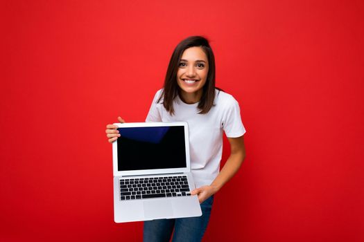 Photo of beautiful young girl holding computer laptop looking at camera isolated over colourful background.