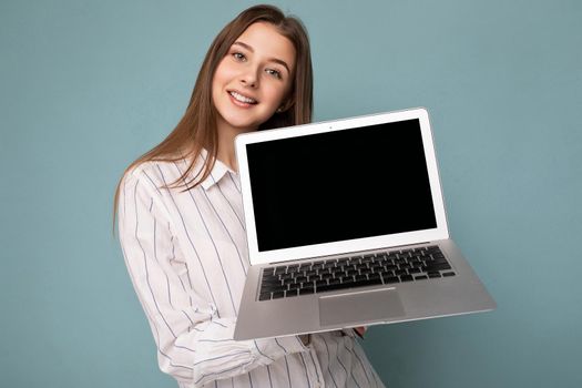 Close-up portrait of Beautiful smiling young woman holding netbook computer looking at camera wearing white shirt isolated on blue background. mock up