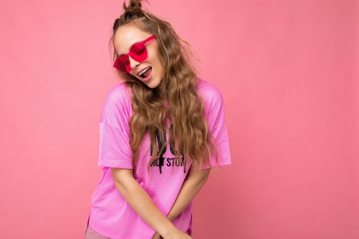 Attractive sexy shy young blonde woman wearing everyday stylish clothes and modern sunglasses isolated on colorful background wall looking down.