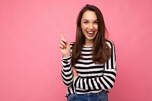 Shot of young positive happy attractive brunette woman with sincere emotions wearing casual striped longsleeve isolated on pink background with empty space and having an idea.
