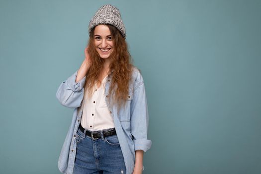Attractive smiling happy young dark blonde woman standing isolated over colorful background wall wearing everyday stylish outfit showing facial emotions looking at camera. Empty space
