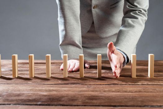 Businesswoman protecting dominoes from falling on wooden desk. Business assistance and leadership in crisis. Operative business solution and stabilization of situation. Professional risk management