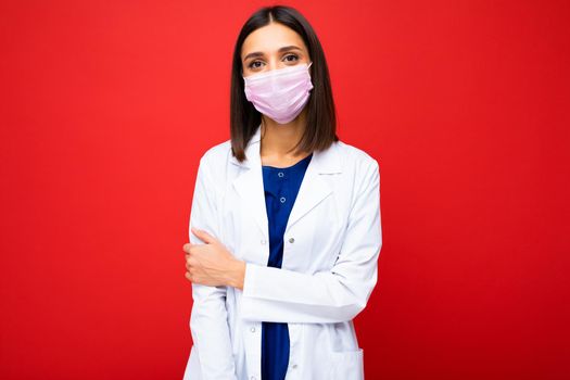 Woman in virus protective mask on face against coronavirus and white medical coat isolated on the background.