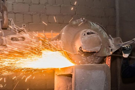 Heavy grinding equipment suspended on a chain with a hook processes and cleans cast iron reinforced concrete tubing in the workshop of an industrial plant.