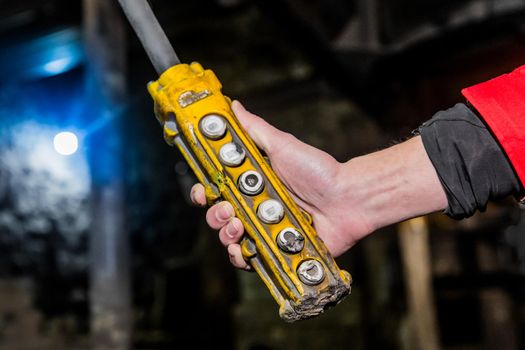 The hand of a working man holds the control panel of the crane lifting mechanism at an industrial plant.