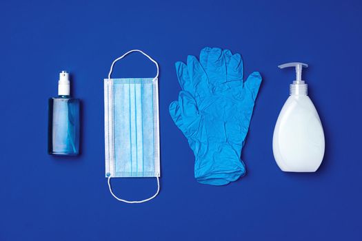 Coronavirus prevention. Facial mask, gloves, soap and sanitizer on blue background close up