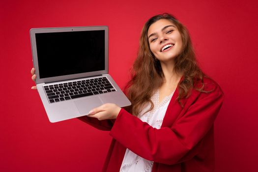 Photo of beautiful young woman holding computer laptop looking at camera isolated over colourful background. Mock up, copy space