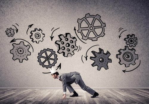 Young handsome businessman wearing white paper crown running and gear mechanism on wall