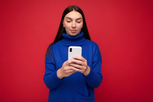 Beautiful young woman wearing casual clothes standing isolated over background surfing on the internet via phone looking at mobile screen.