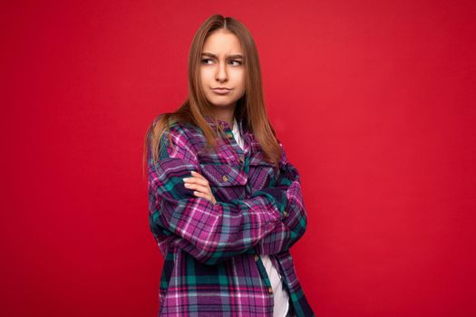 Photo shot of attractive sexy touchy upset young dark blonde woman isolated over red background wall wearing purple stylish shirt looking to the side keeping cross hands. copy space