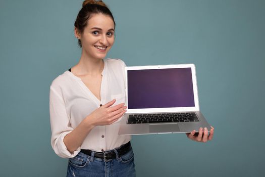 Close-up portrait of Beautiful happy young woman holding computer laptop looking at camera having fun pointing at netbook display wearing casual smart clothes isolated over wall background. Mock up, copy space