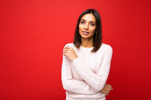 Portrait of positive cheerful cute smiling young brunette woman in casual sweater isolated on red background with copy space.