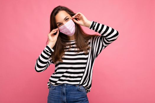 Shot of positive young attractive woman wearing mediacal face mask isolated over background wall. Protection against COVID-19. Empty space