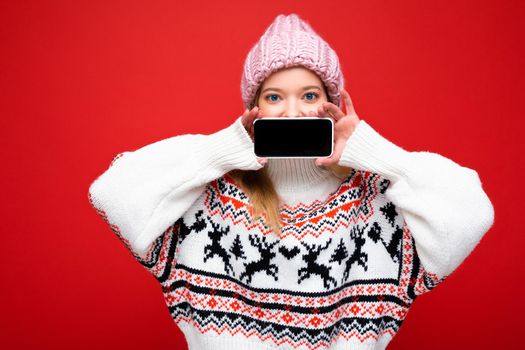Photo of beautiful smiling young woman good looking wearing casual stylish outfit standing isolated on background with copy space holding smartphone showing phone in hand with empty screen display for mockup looking at camera.