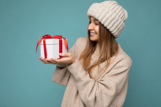 Shot of attractive positive smiling young dark blonde woman isolated over colourful background wall wearing everyday trendy outfit holding gift box and looking to the side. Copy space, mockup