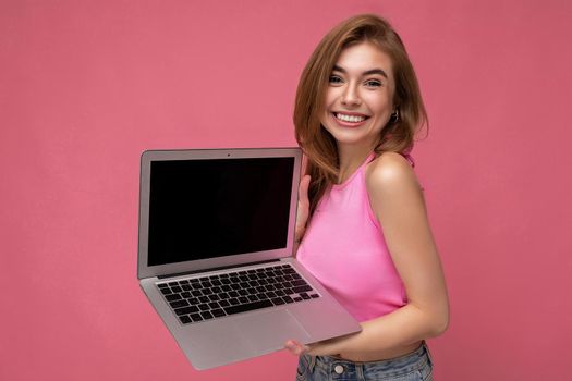 Photo of beautiful young girl holding computer laptop looking at camera isolated over colourful background.
