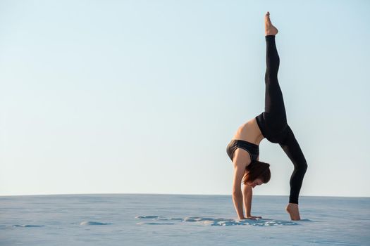 Young woman practicing inversion balancing yoga pose handstand on sand. Sunset and white sand.