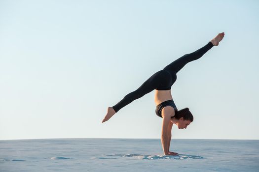 Young woman practicing inversion balancing yoga pose handstand on sand. Sunset and white sand.