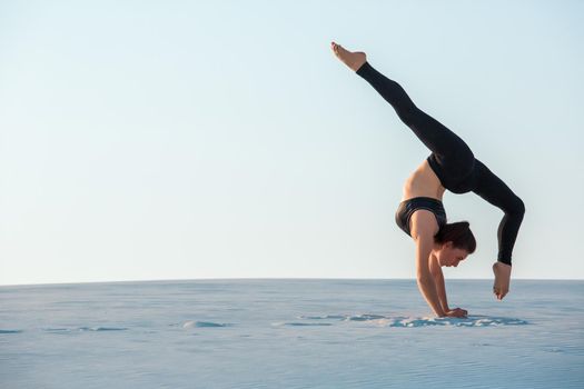 Young woman practicing inversion balancing yoga pose handstand on sand. Sunset and white sand.