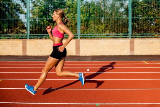 Side view beautiful young woman exercise jogging and running on athletic track on stadium. Sport, healthy lifestyle concept.