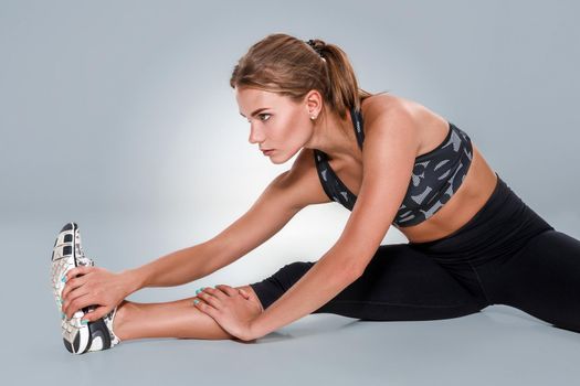 Stretching workout posture by a woman on studio gray background. Sports lifestyle