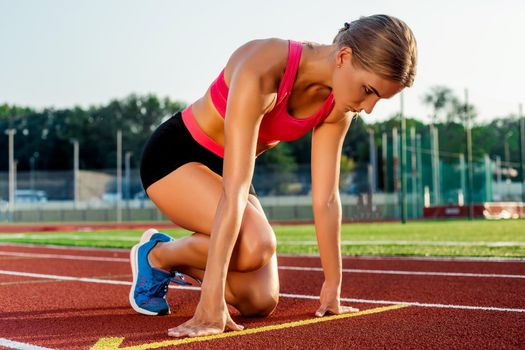 Young woman athlete at starting position ready to start a race. Female sprinter ready for sports exercise on racetrack.