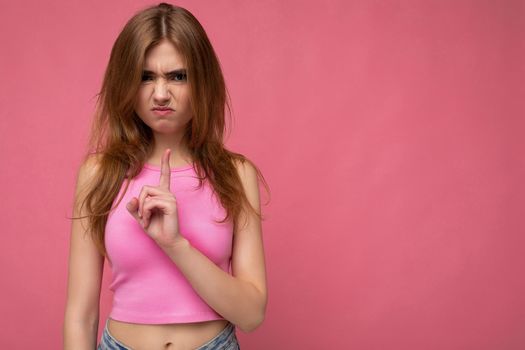 Dissatisfied young beautiful dark blonde woman with sincere emotions isolated on background wall with copy space wearing stylish pink top. Negative concept.