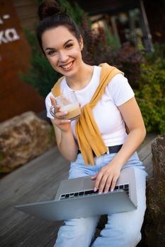 woman student studying on the street sitting with a laptop on her lap.