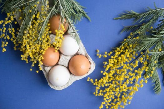 Easter background, eggs and a wooden hare on a blue background, decorated with Mimosa flowers, flatlay, top view, empty space for text. happy Easter.