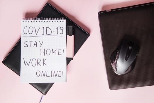 Top view of a desktop with laptops, a marker, and a laptop. Text Covid-19, stay at home, WORK ONLINE. Work from home using an online device, protection from coronavirus during the quarantine period. Pink background. Flat lay.