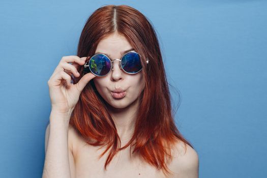 perky red-haired woman in blue glasses bare shoulders posing. High quality photo