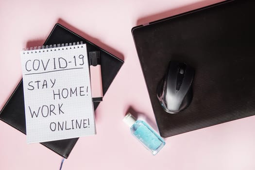 Top view of a desktop with laptops, a marker, and a laptop. Text Covid-19, stay at home, WORK ONLINE. Work from home using an online device, protection from coronavirus during the quarantine period. Pink background. Flat lay.