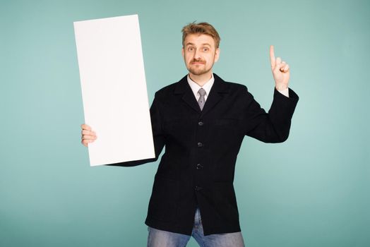 Happy smiling young business man showing blank signboard, on blue background