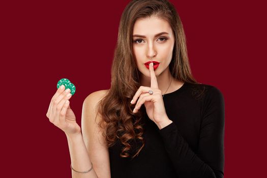 Pretty long hair woman in black dress holding chips for gambling in casino. Studio shot on red background. Poker. Two green Chips in Hand