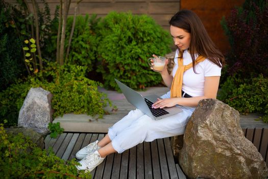 young brunette woman in casual clothes resting outside while drinking coffee.