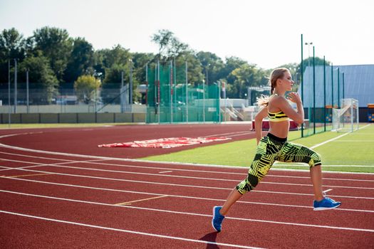 Beautiful young woman exercise jogging and running on athletic track on stadium. Red treadmill in sport field.