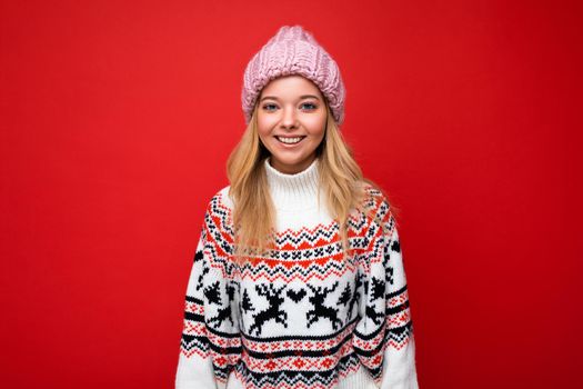 Attractive smiling happy young blonde woman standing isolated over colorful background wall wearing everyday stylish outfit showing facial emotions looking at camera.