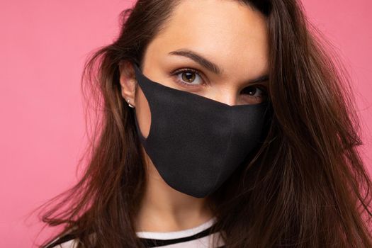 Closeup shot of of young fascinating woman wearing mediacal face mask isolated over background wall. Protection against COVID-19.