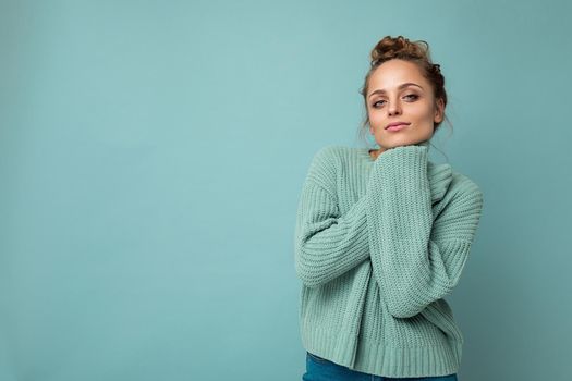 Portrait of young happy positive satisfied cute cozy attractive beautiful blonde woman with sincere emotions wearing casual blue pullover isolated on blue background with copy space.