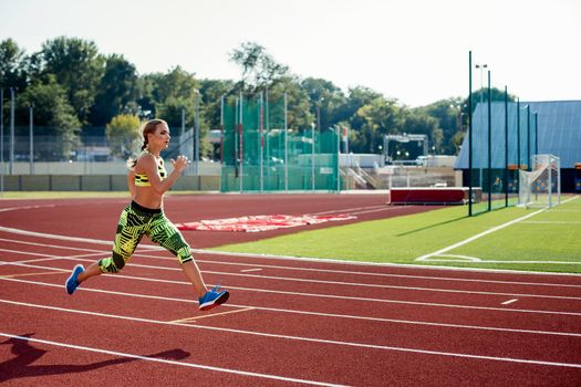 Beautiful young woman exercise jogging and running on athletic track on stadium. Red treadmill in sport field.