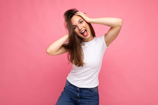 Young beautiful brunet woman. Trendy lady in casual summer white t-shirt for mock up. Positive female shows facial sincere emotions. Funny model isolated on pink background with free space.