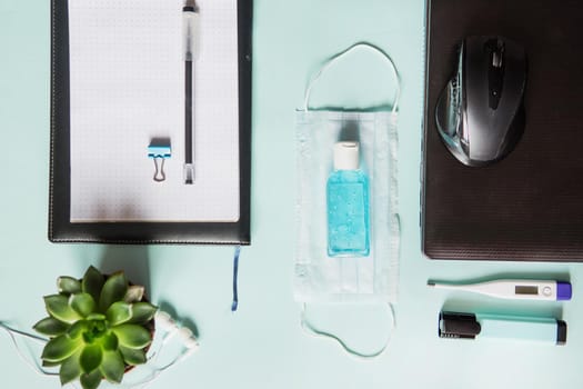 Top view of a desktop with notebooks, pens, and a laptop. Work from home using an online device, protection from coronavirus during the quarantine period. Protective masks and antiseptic on a mint background.