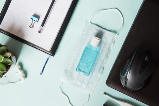 Top view of a desktop with notebooks, pens, and a laptop. Work from home using an online device, protection from coronavirus during the quarantine period. Protective masks and antiseptic on a mint background.