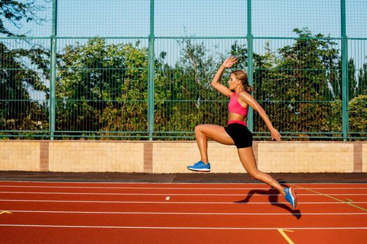 Side view beautiful young woman exercise jogging and running on athletic track on stadium. Sport, healthy lifestyle concept.