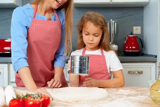 Mother and her little daughter preparing dough in kitchen close up