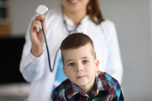 Doctor pediatrician holding stethoscope near little boy in clinic. Pediatrics treatment of children concept